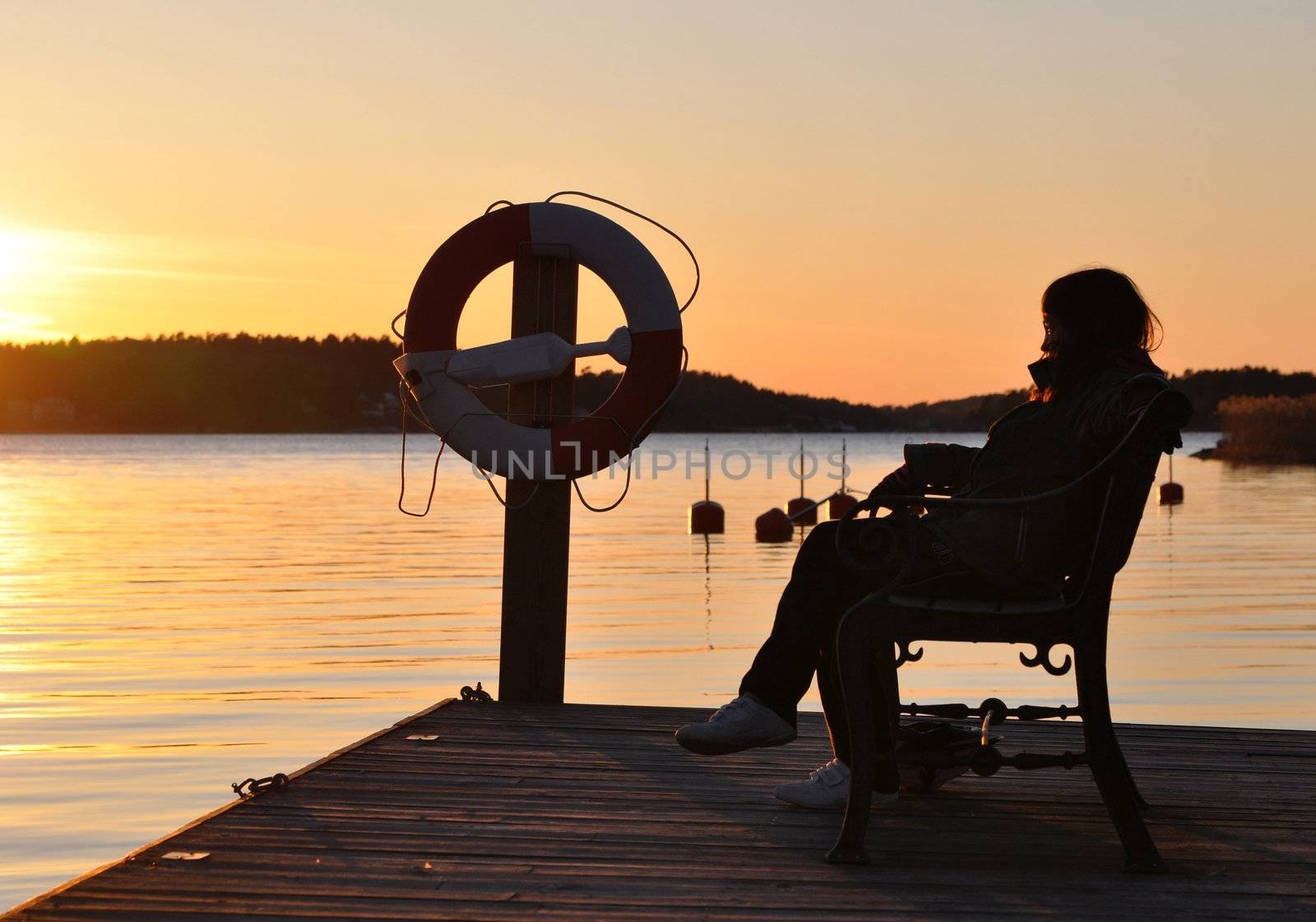 A girl sitting on a bench on a bridge during sunset in the archipelago of Stockholm.