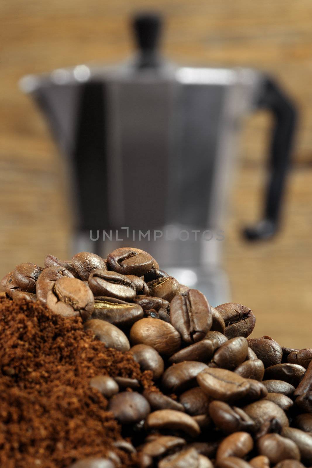 Image of an Italian Moka Express stovetop coffee maker behind coffee beans and grinds.  Shallow depth of field - focus is on top layer of beans.
