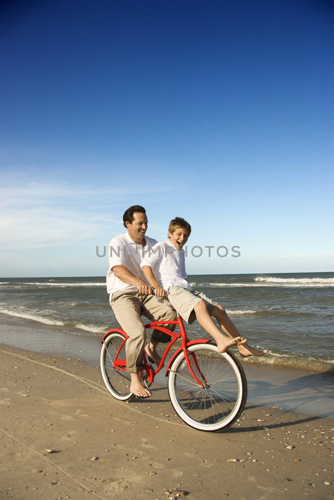 Caucasian father on bicycle with pre-teen boy riding on handlebars.