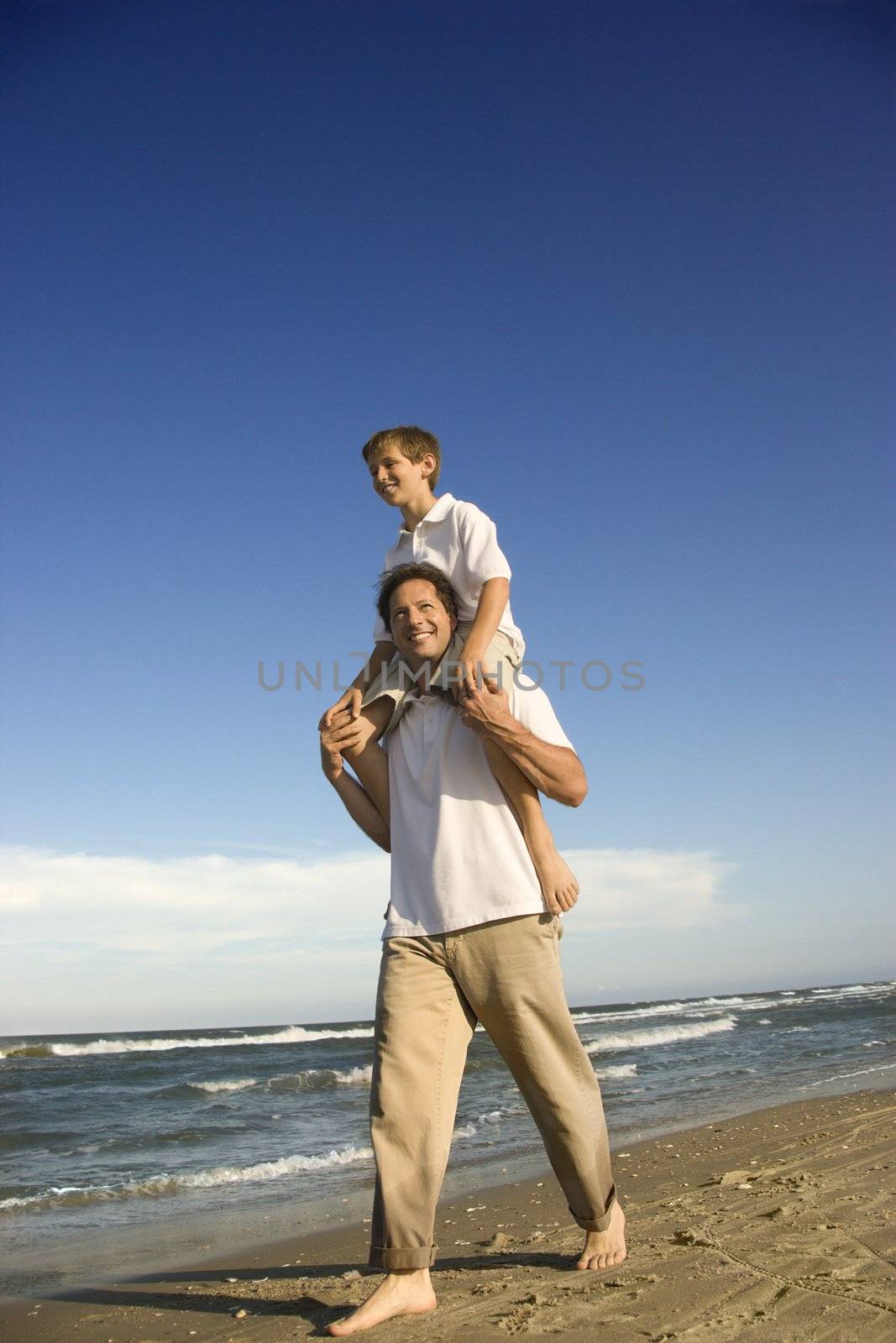 Caucasian father with pre-teen boy on shoulders on beach.