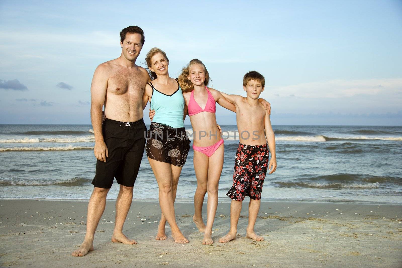 Caucasian family of four standing on beach.