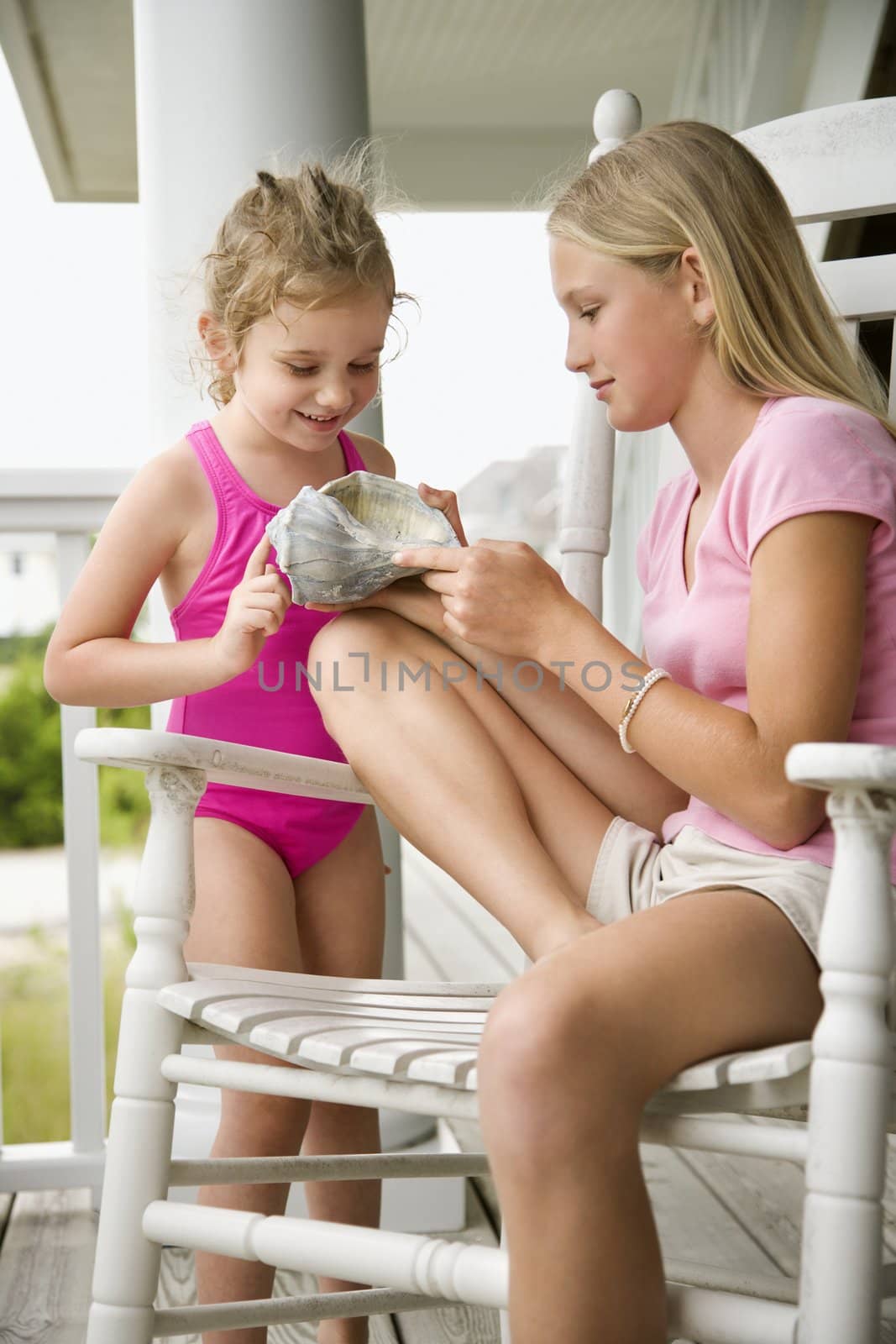 Caucasian pre-teen girl showing conch shell to other Caucasian female child.