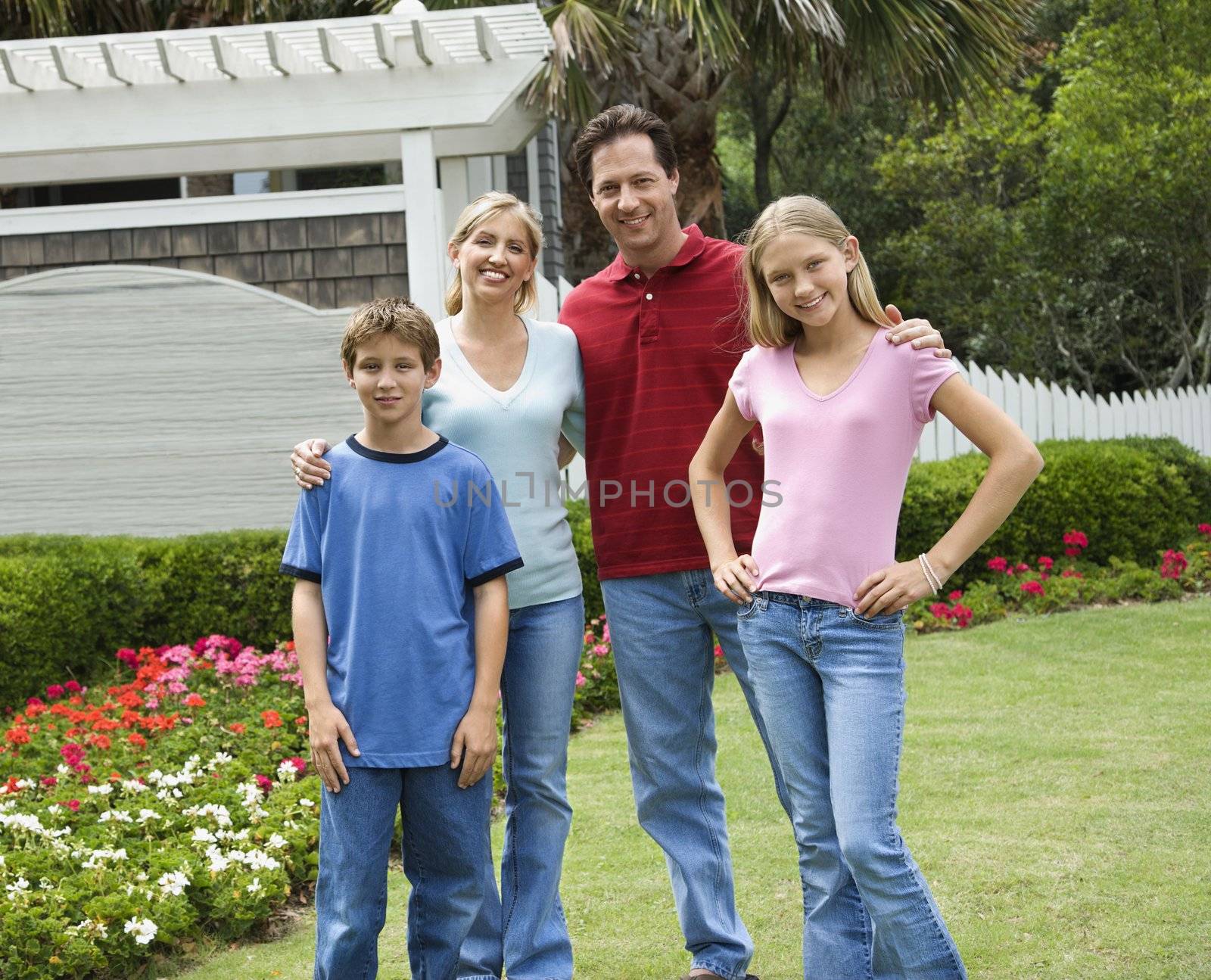 Caucasian family of four posing for portrait in yard.
