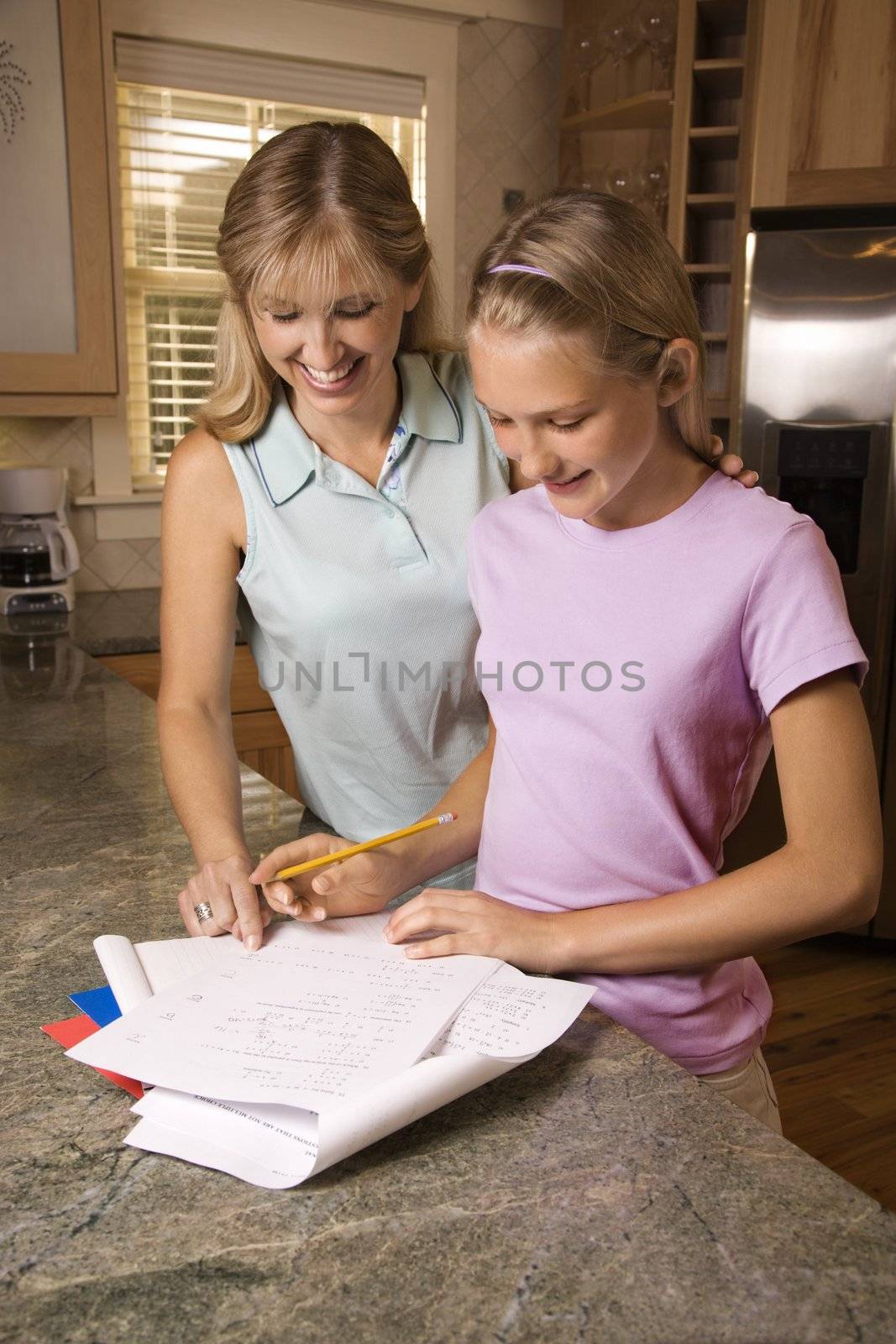 Caucasian mid-adult mother helping pre-teen daughter with homework at kitchen counter.