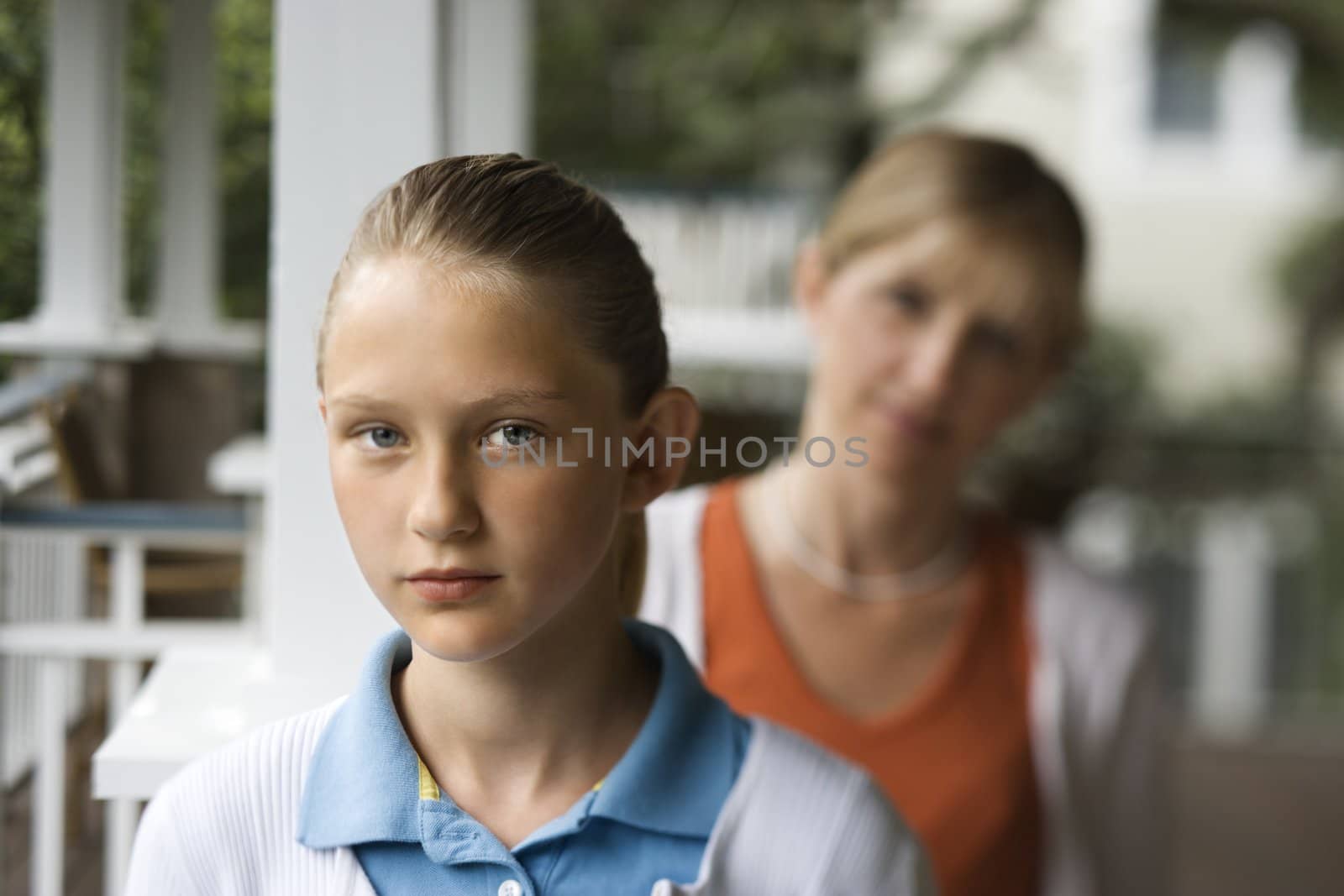 Caucasian pre-teen girl with mother behind her looking over shoulder.