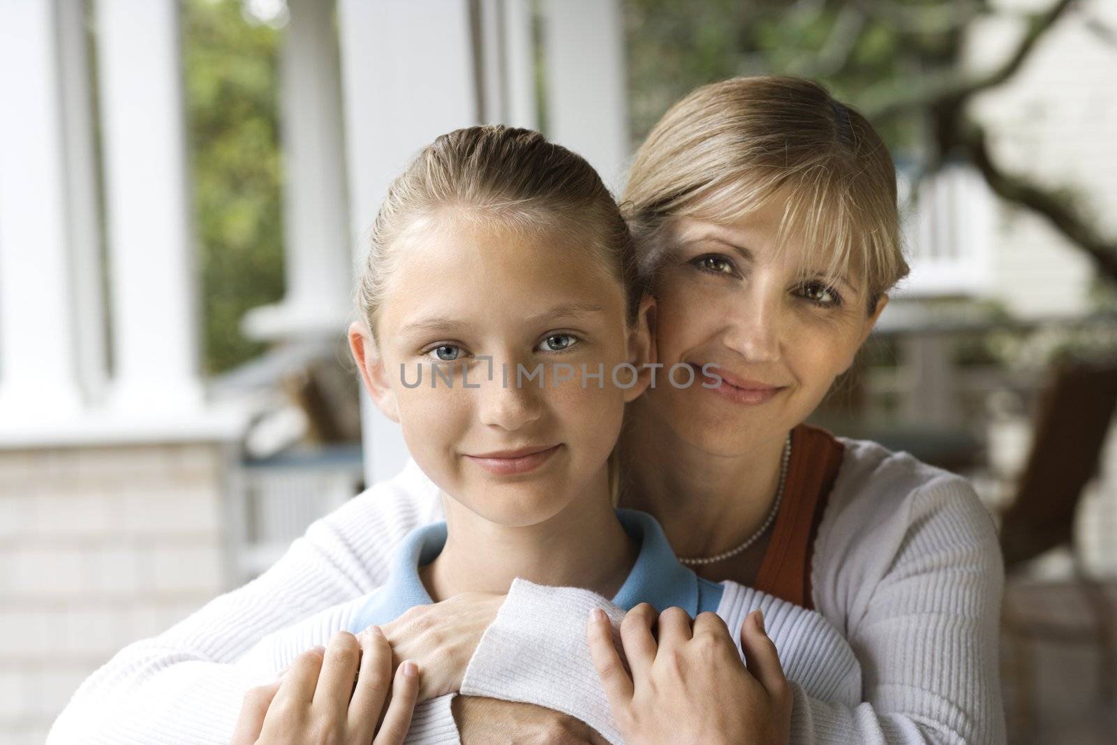 Caucasian mid-adult mother hugging pre-teen daughter.