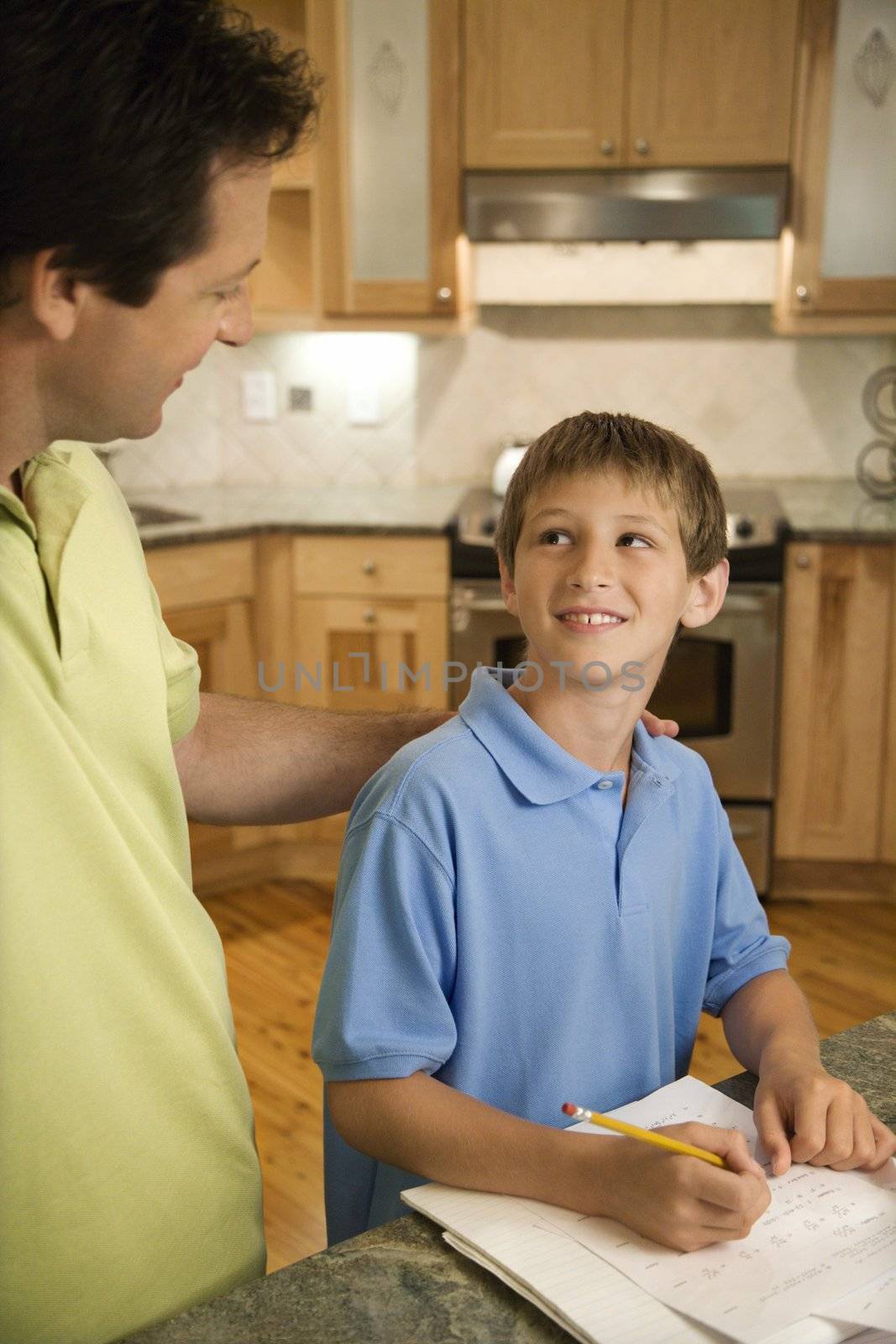 Caucasian mid-adult father helping pre-teen son with homework in kitchen.