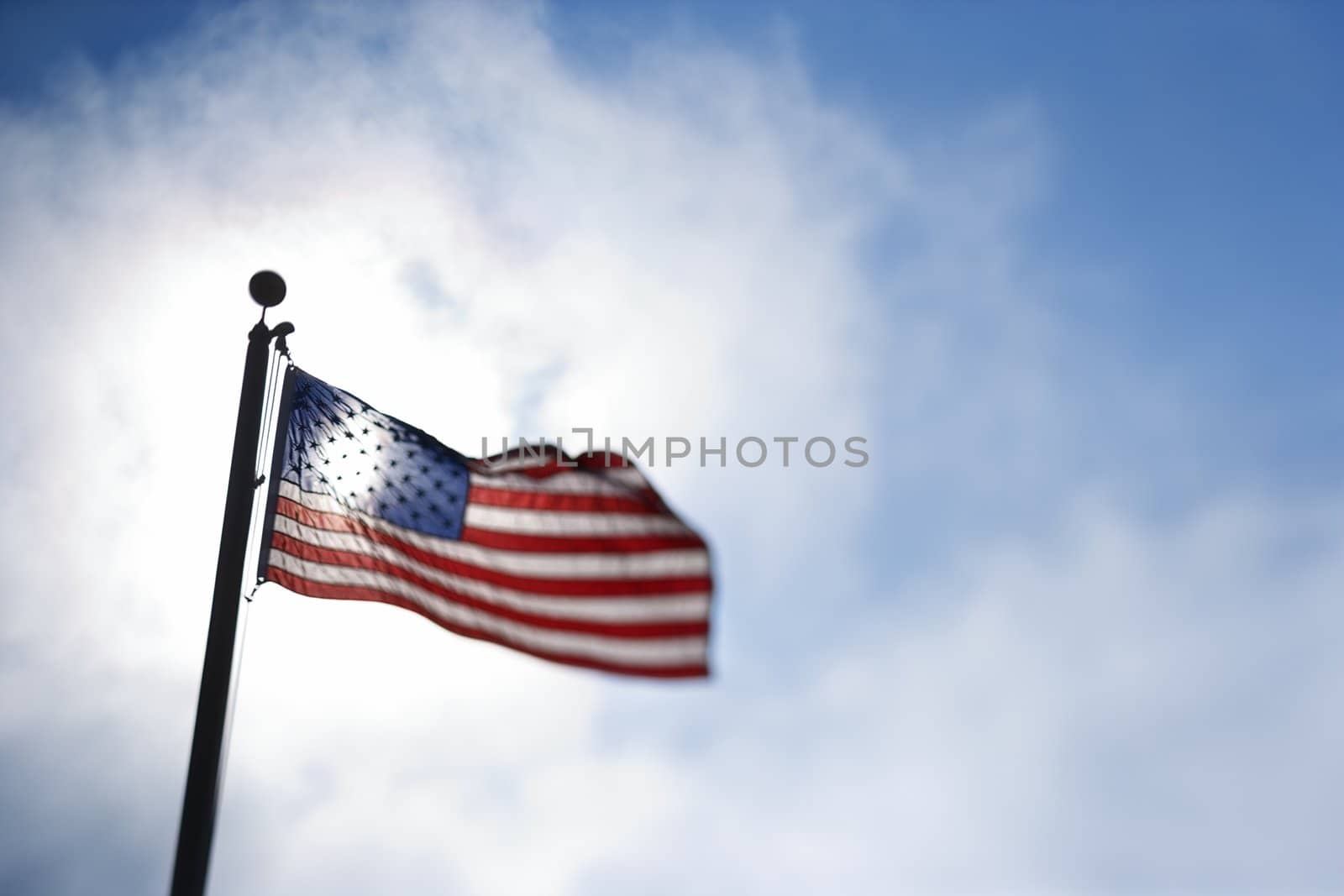 American flag blowing in breeze against blue sky.