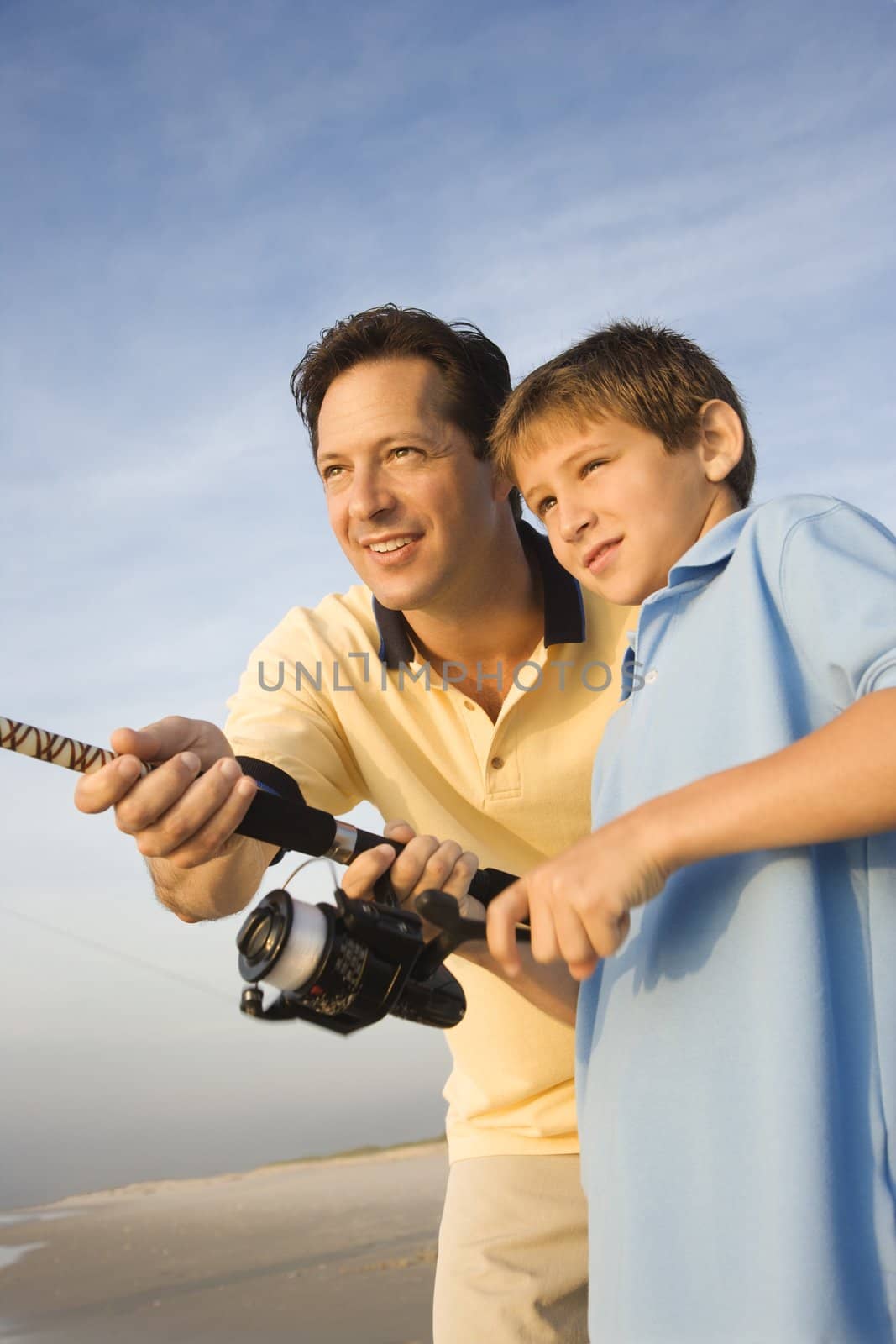 Caucasian mid-adult man shore fishing on beach with pre-teen boy