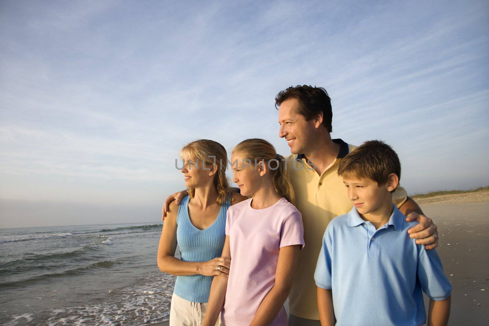 Portrait of Caucasian family of four posing on beach looking at ocean.