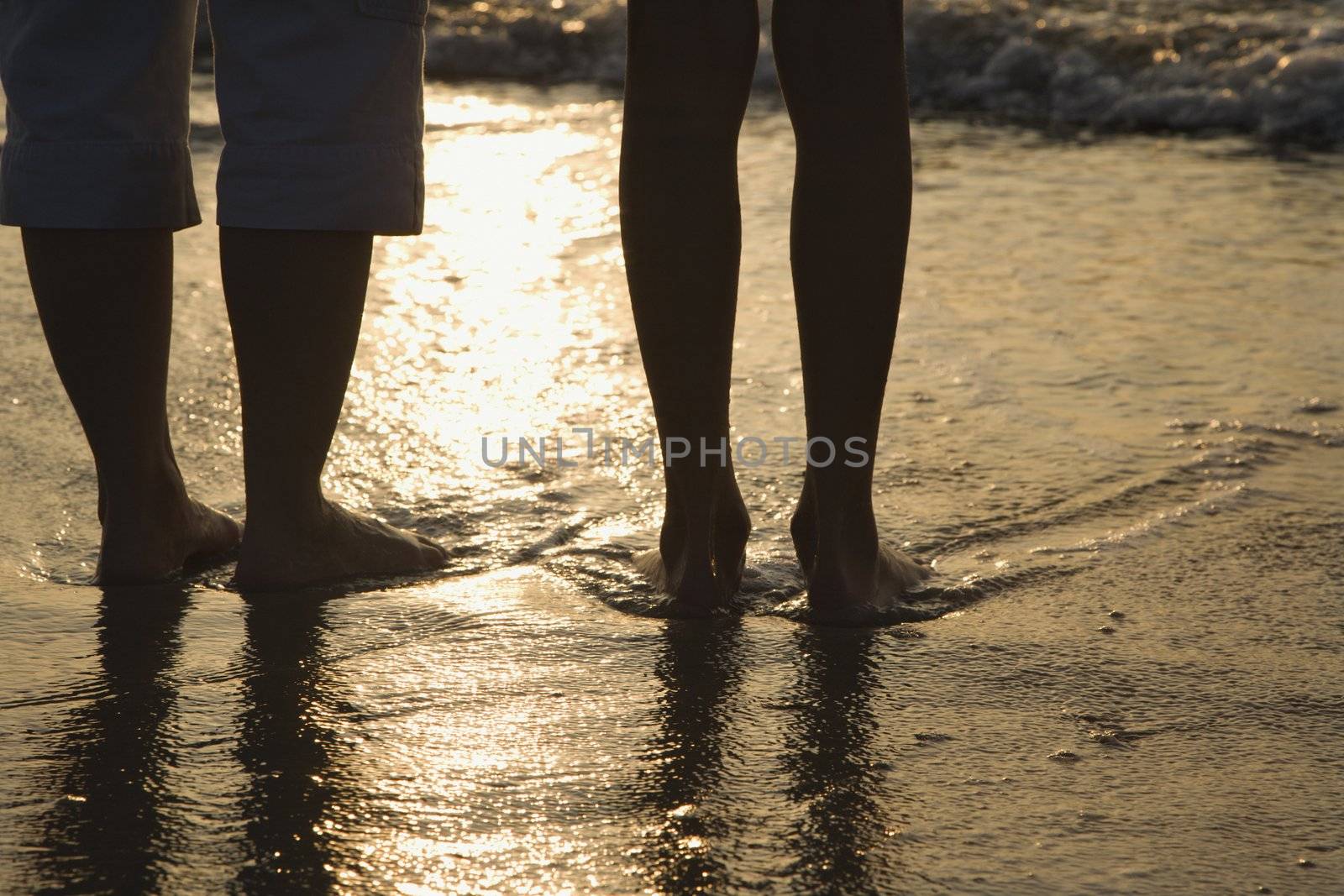 Caucasian women standing barefoot on beach in water.