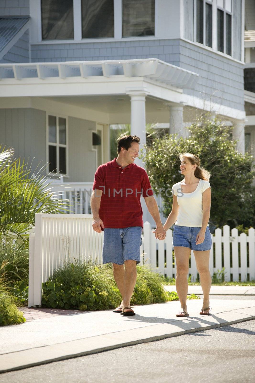 Caucasian mid-adult couple walking on suburban sidewalk holding hands.