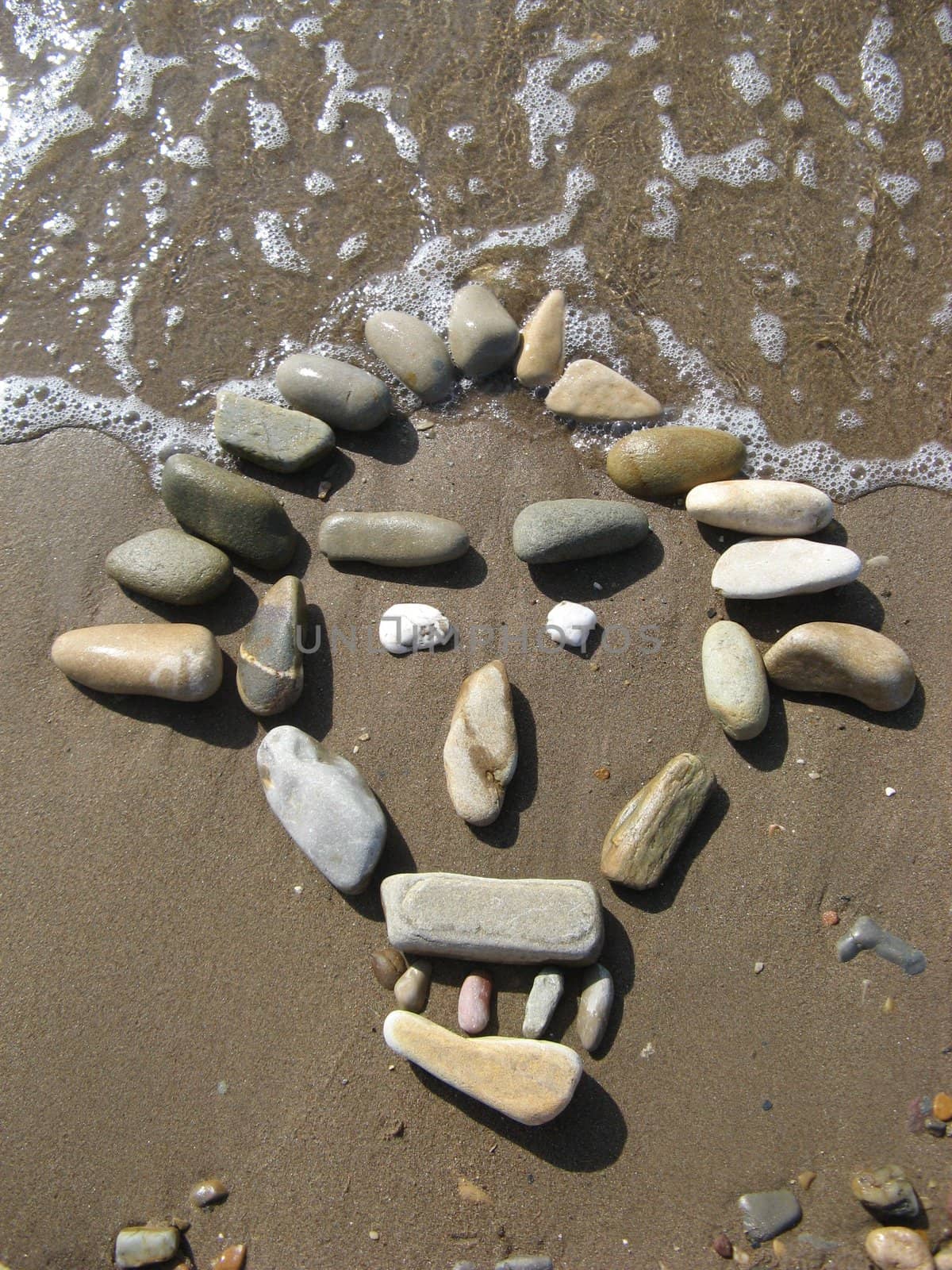 african mask drawed with pebbles on the beach