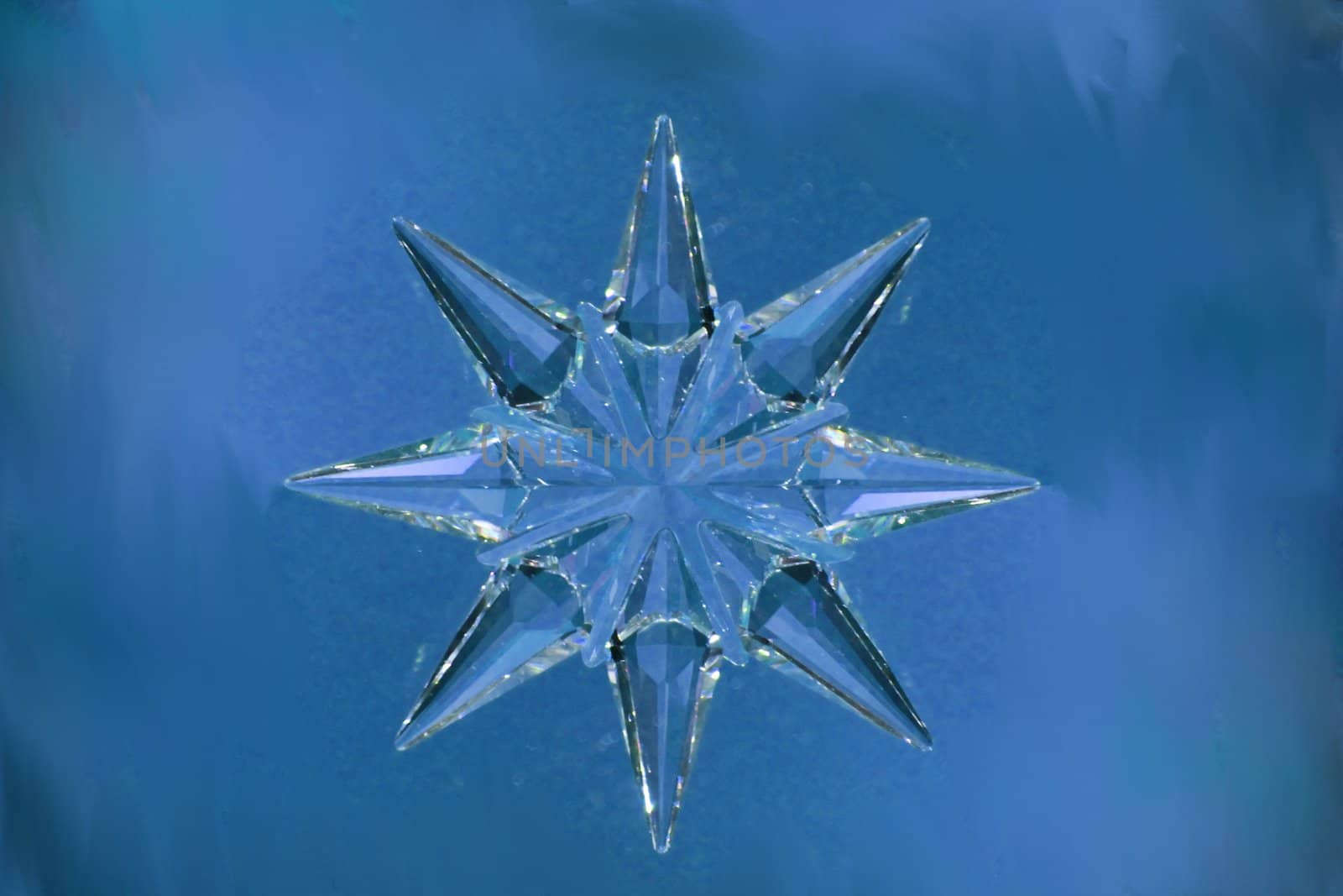 A Christmas ornament made of crystal in a star or snow flake shape with a blue, frost like background.