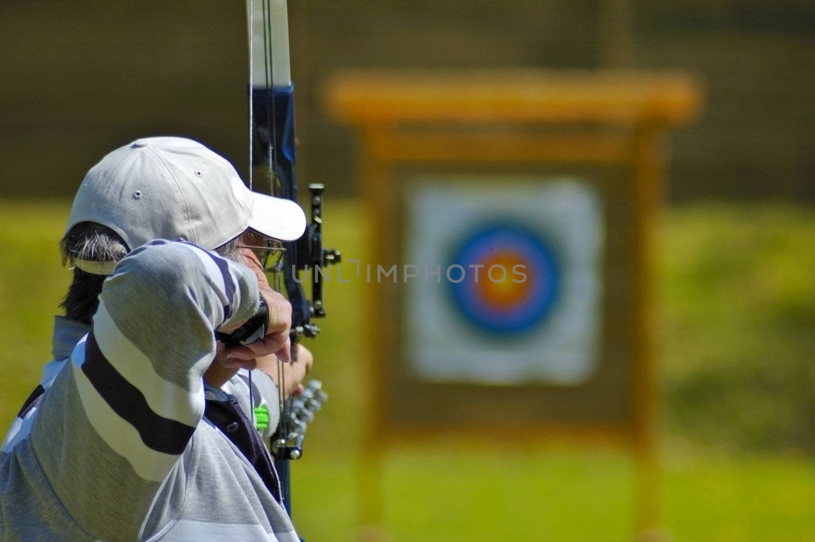 An archer aims at the bullseye of a distant target. Selective focus on the archer's head.