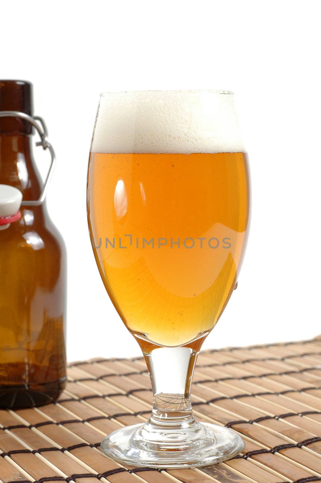 Glass of cold beer with bottle in background.