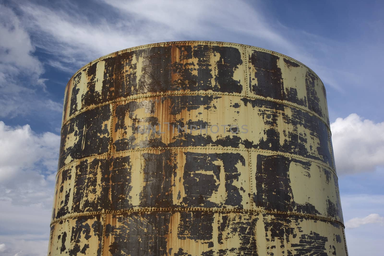 old rusty grain bin or storage tank (metal with rivets design) against partially cloudy sky
