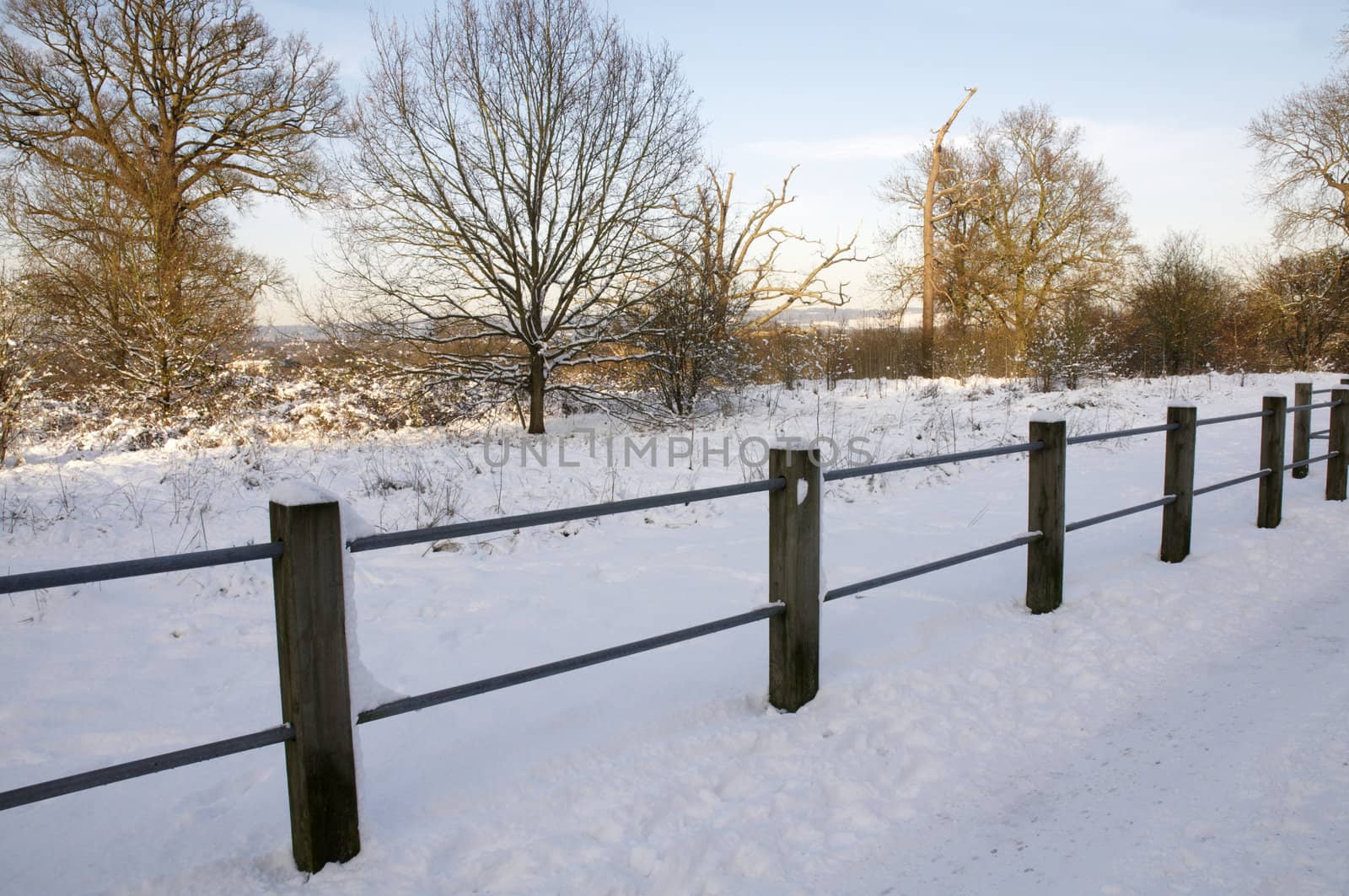 A footpath covered in snow with a fence