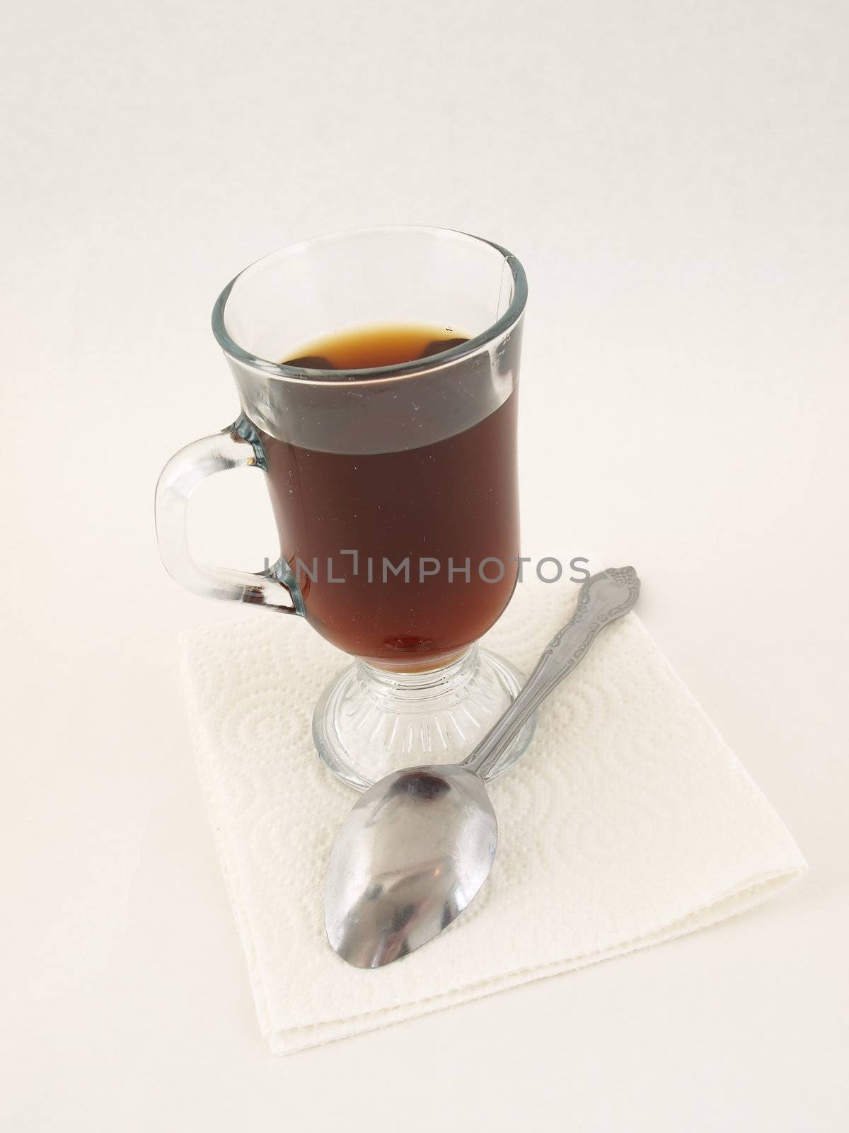 A glass of hot coffee and a silver tablespoon over a white background.