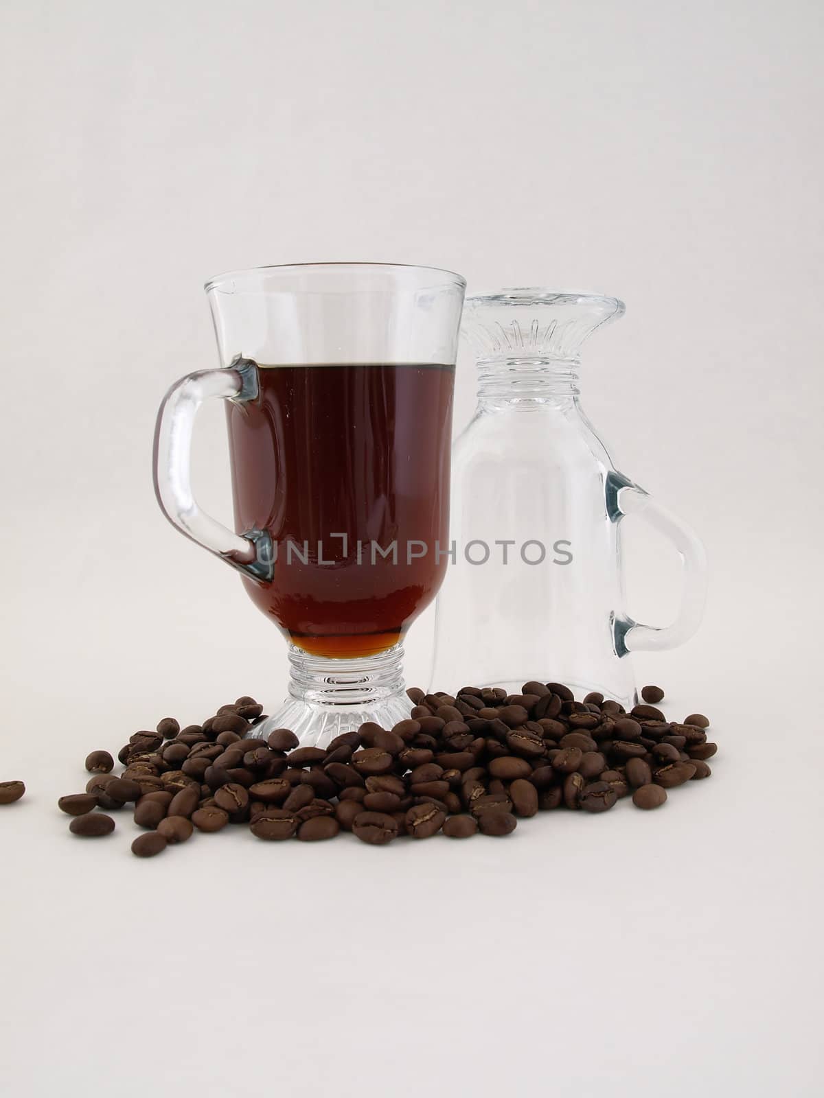 A hot glass of coffee sits next to an inverted glass amongst coffee beans. Isolated on a white background.
