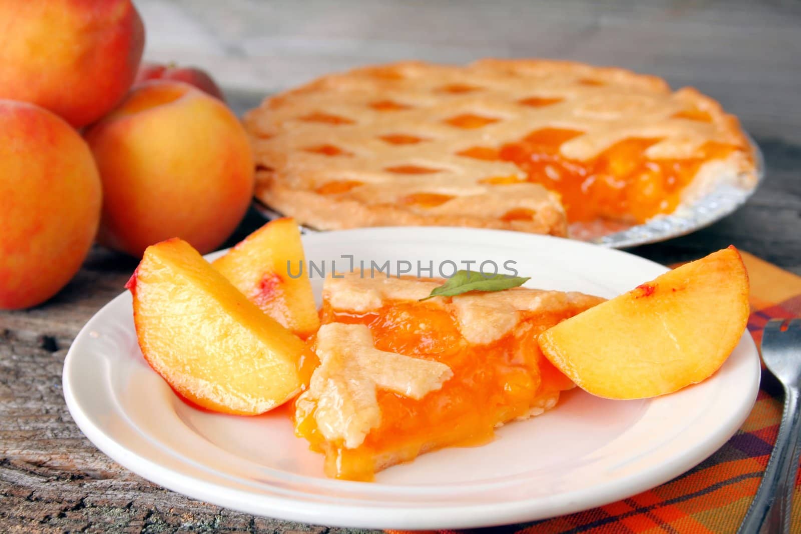 A slice of peach pie, with the pie in the background, and fresh peaches top the image off.