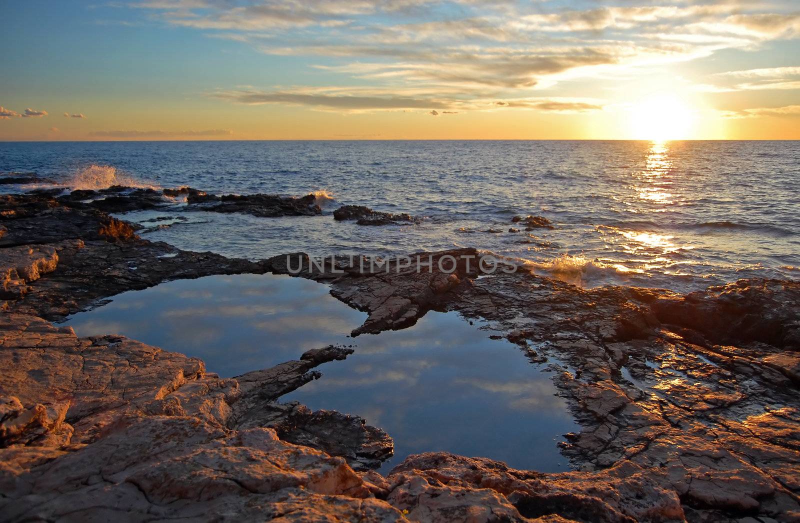 Sunset on a rocky coastline with a puddle