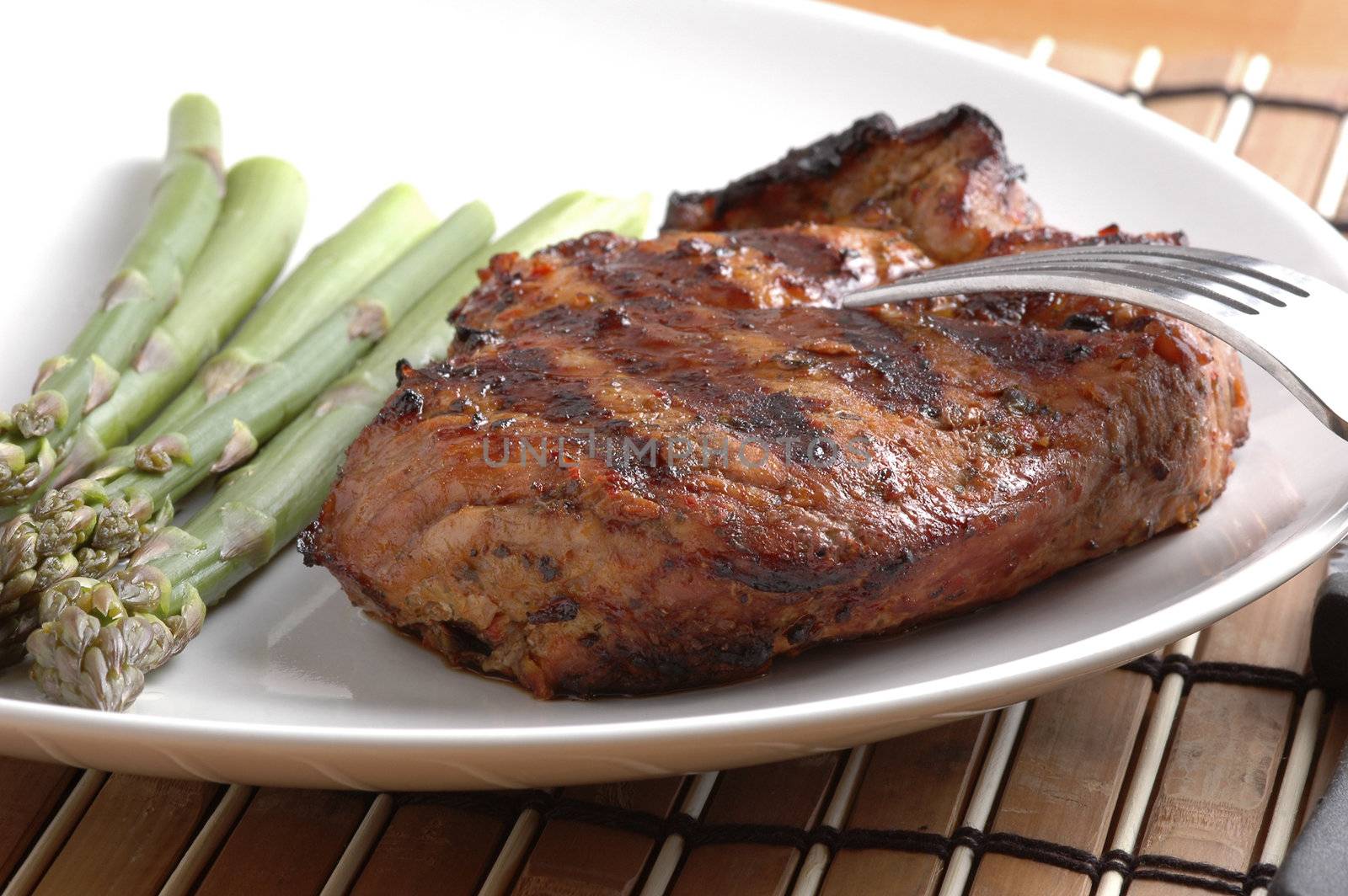 Perfectly grilled pork chop on a plate with asparagus.