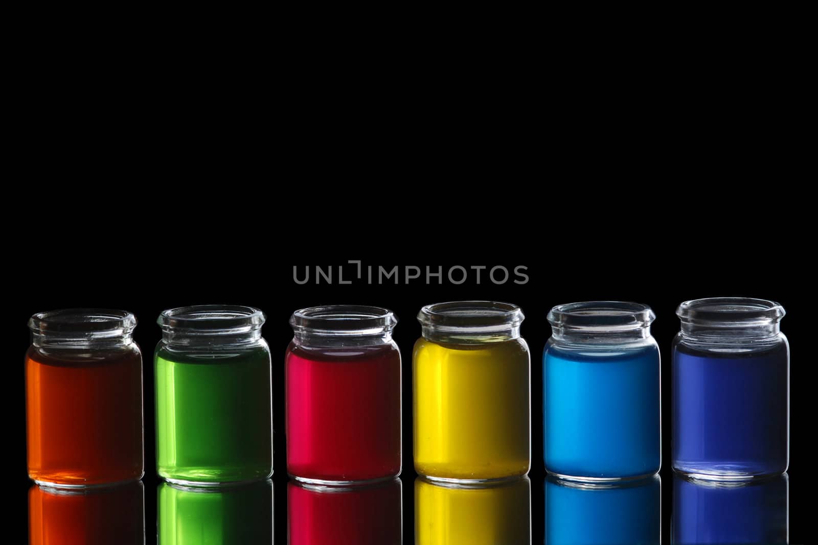 Line of glasses filled with colorful liquid isolated on black background with reflection.
