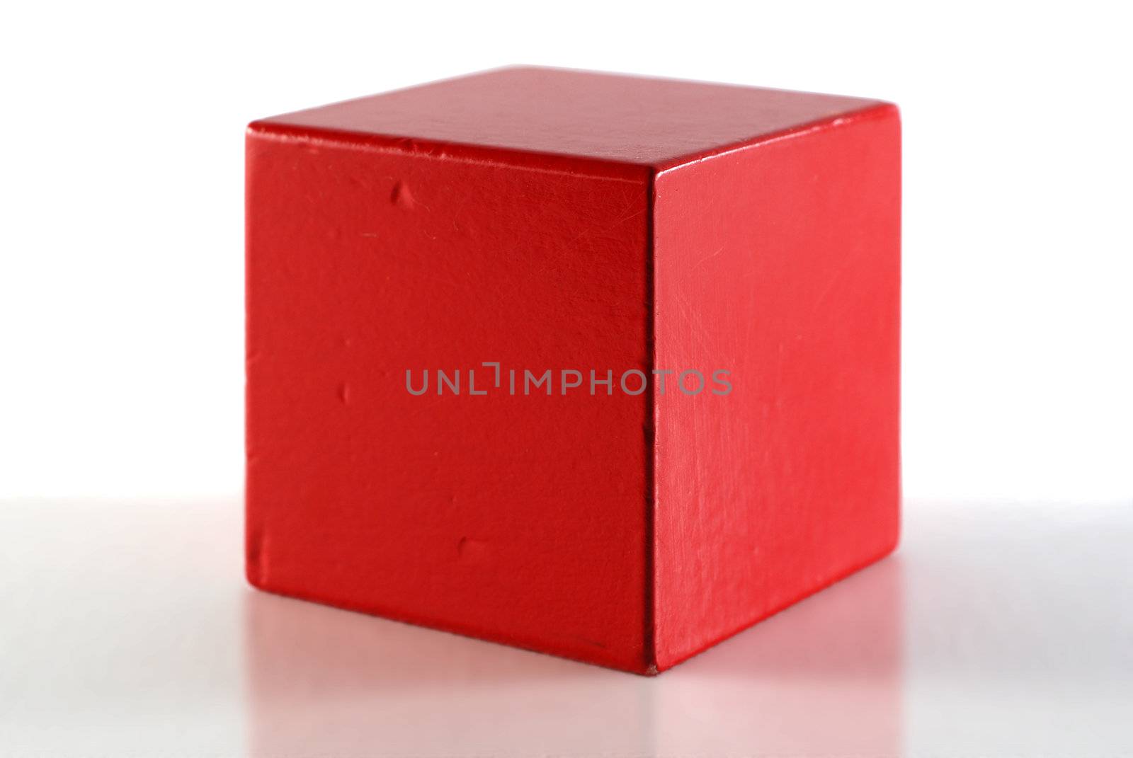 Single red cube on reflective surface. White backround.