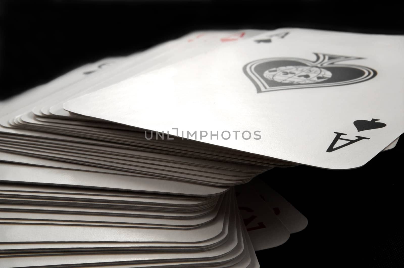 Close and low level focussing on the top card of a stack of playing cards with black background.