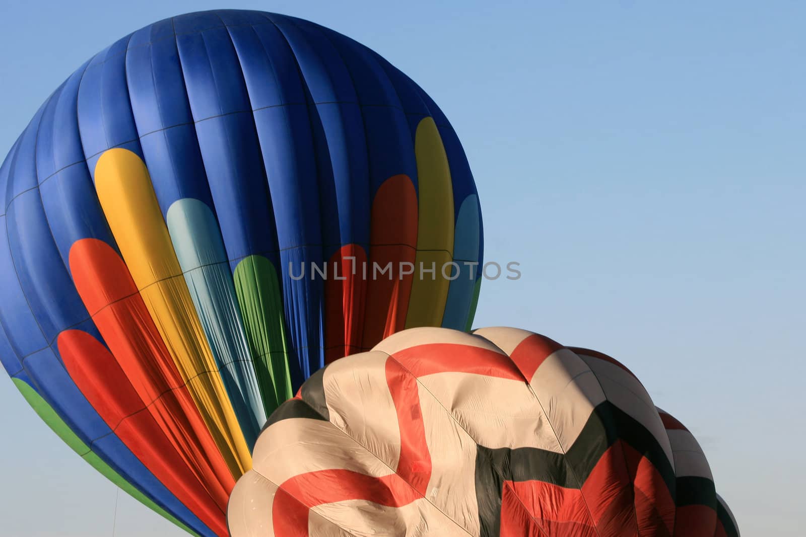 Colorful hot-air balloons inflate against a beautiful bright blue sky