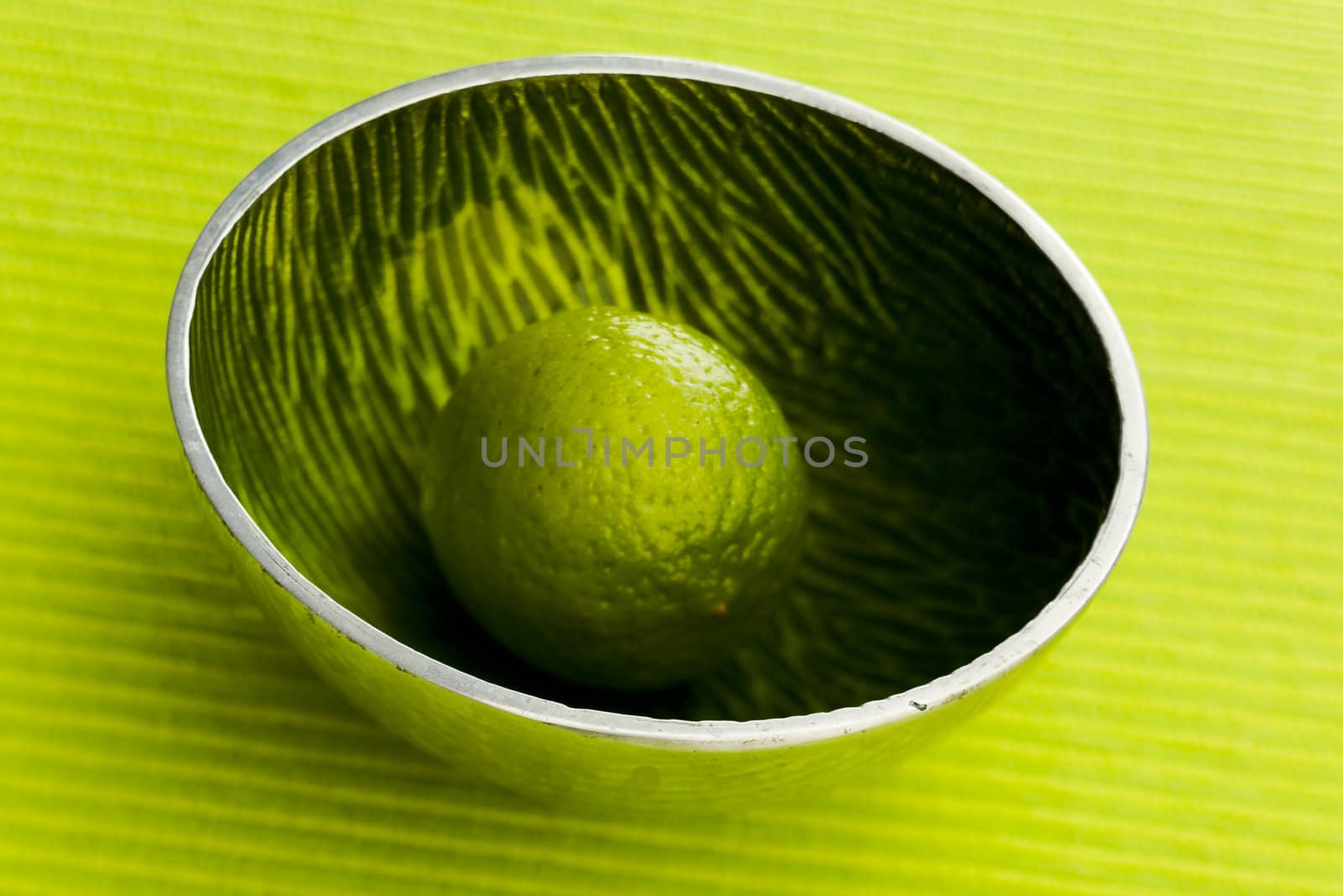 One lime on the small metal bowl over green background