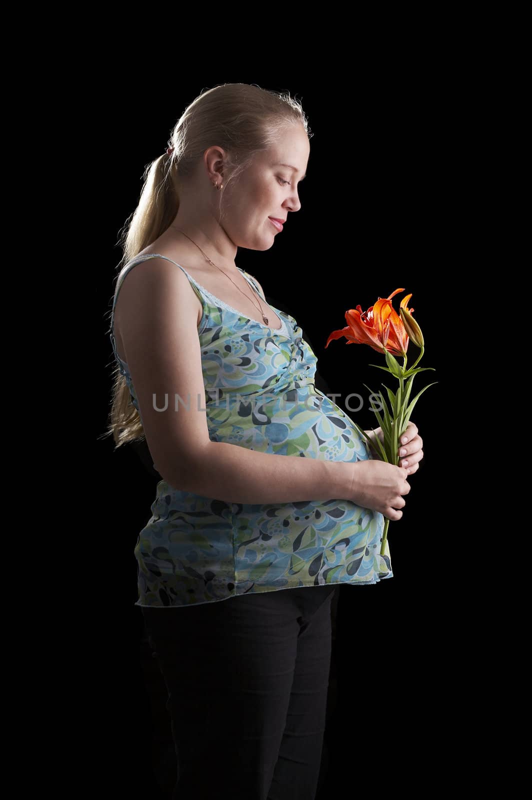 A pregnant young woman holding flower on a black background.