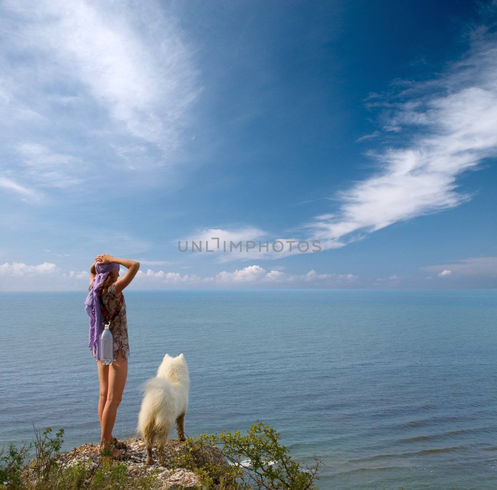 Girl with bottle and samoyed dog standing on precipice above sea