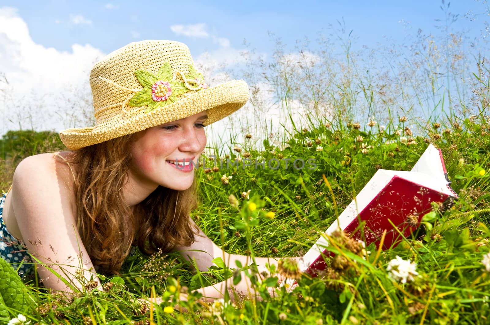 Portrait of teenage girl reading book in summer meadow with straw hat