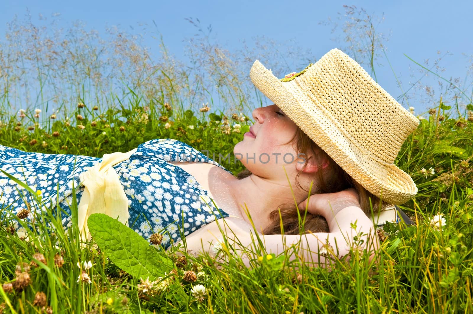 Young teenage girl resting on summer meadow in straw hat