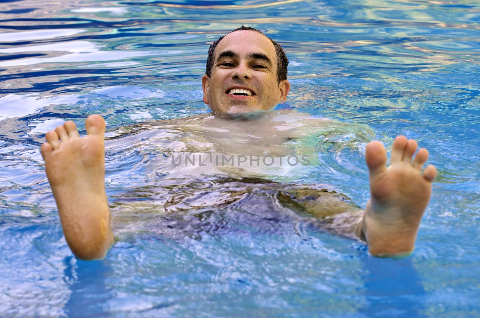 Portrait of a happy man in a swimming pool with feet up