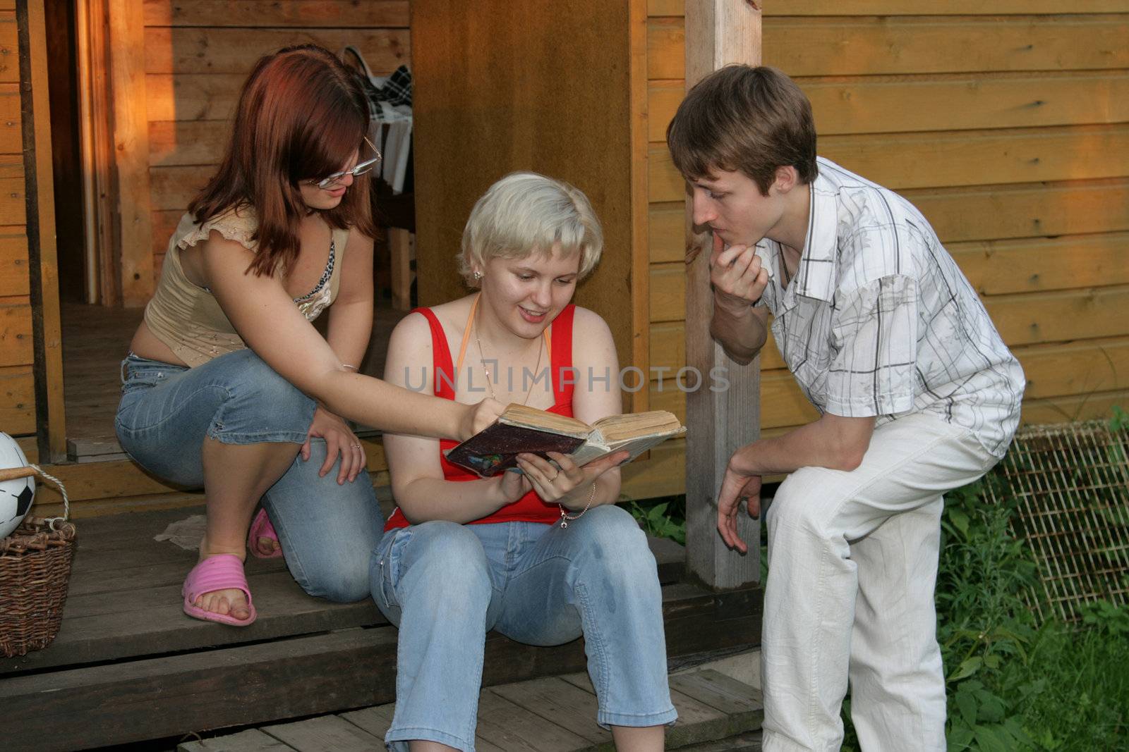 Three friends read the book on a porch of the house
