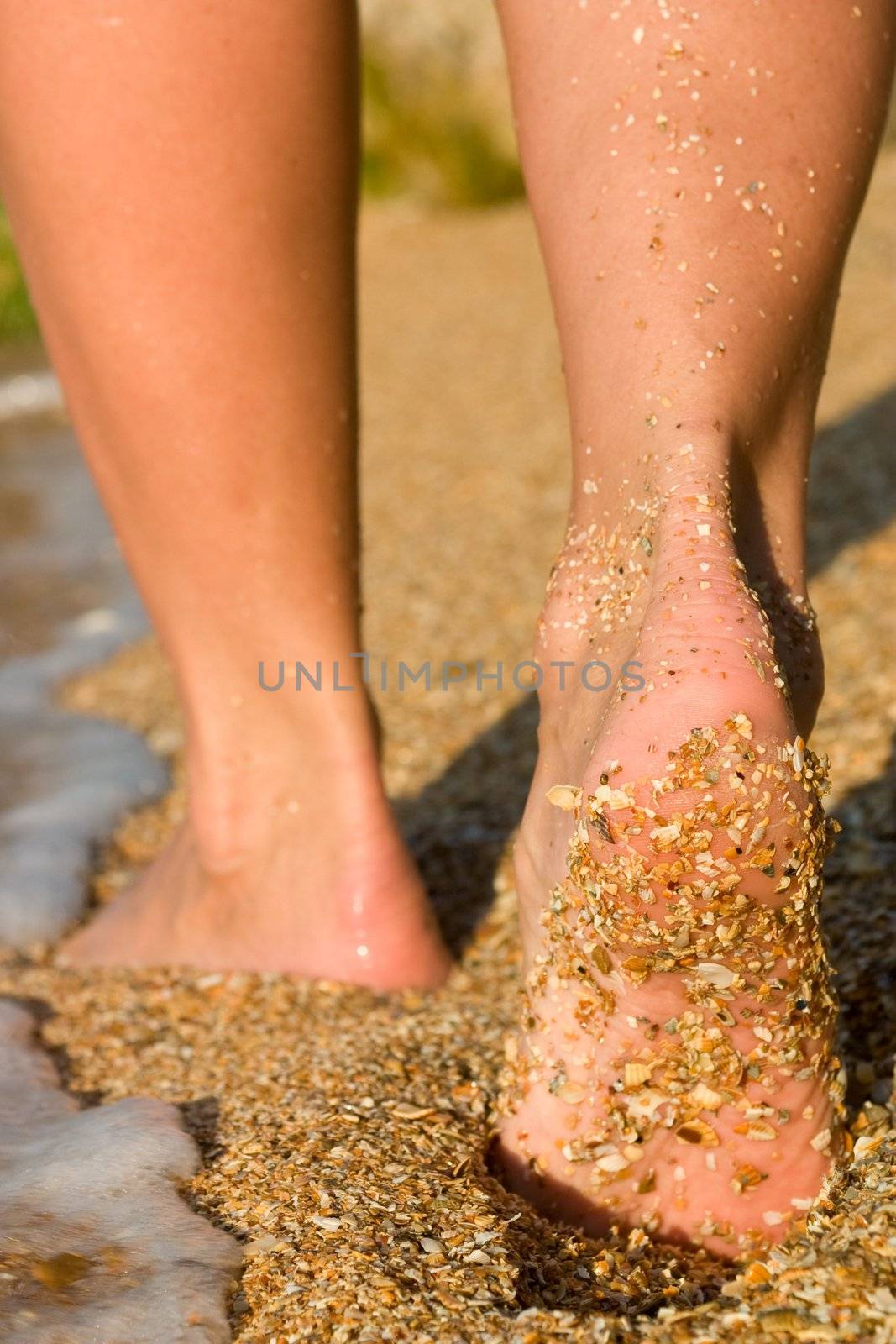 Girl's barefoot feet on beach in sea surf