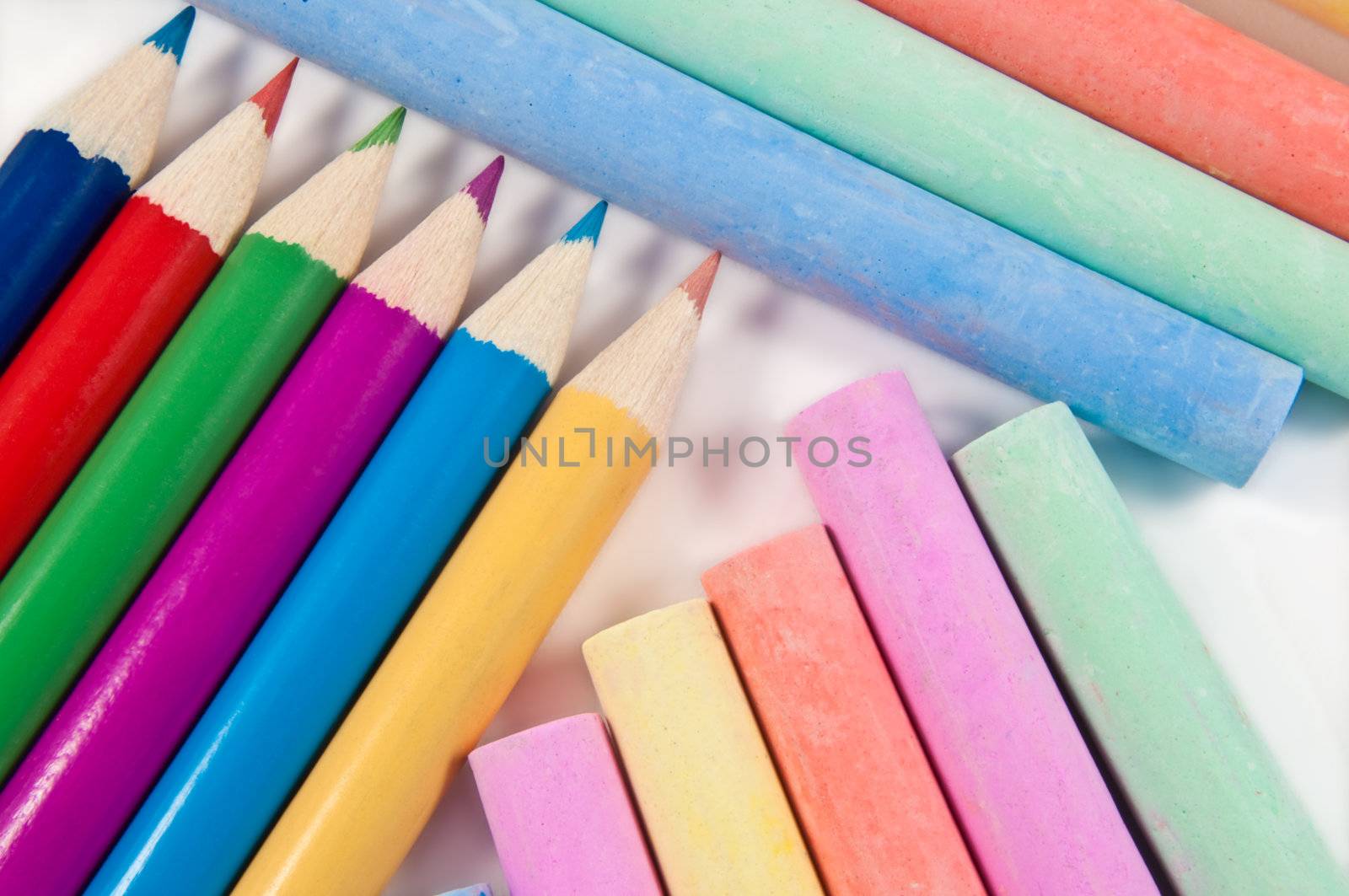 Close up capturing a selection of coloured chalks and pencils arranged over white.