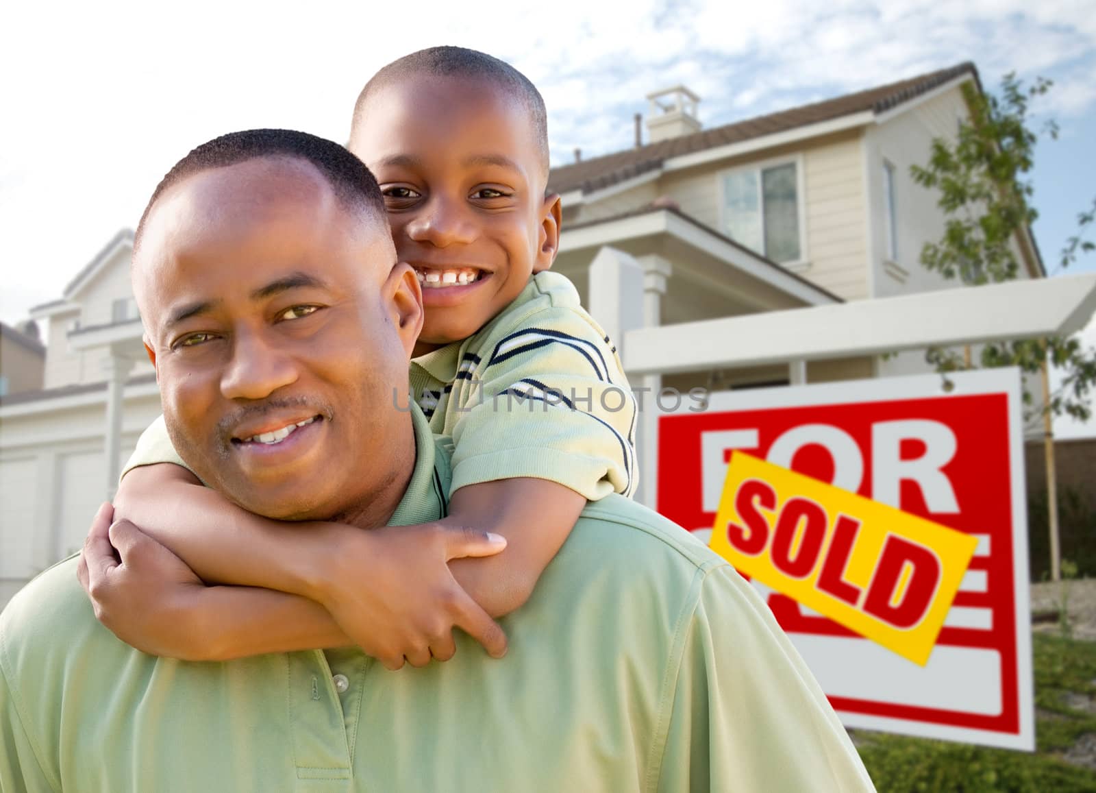 Happy African American Father and Son in Front of New Home and Real Estate Sign.