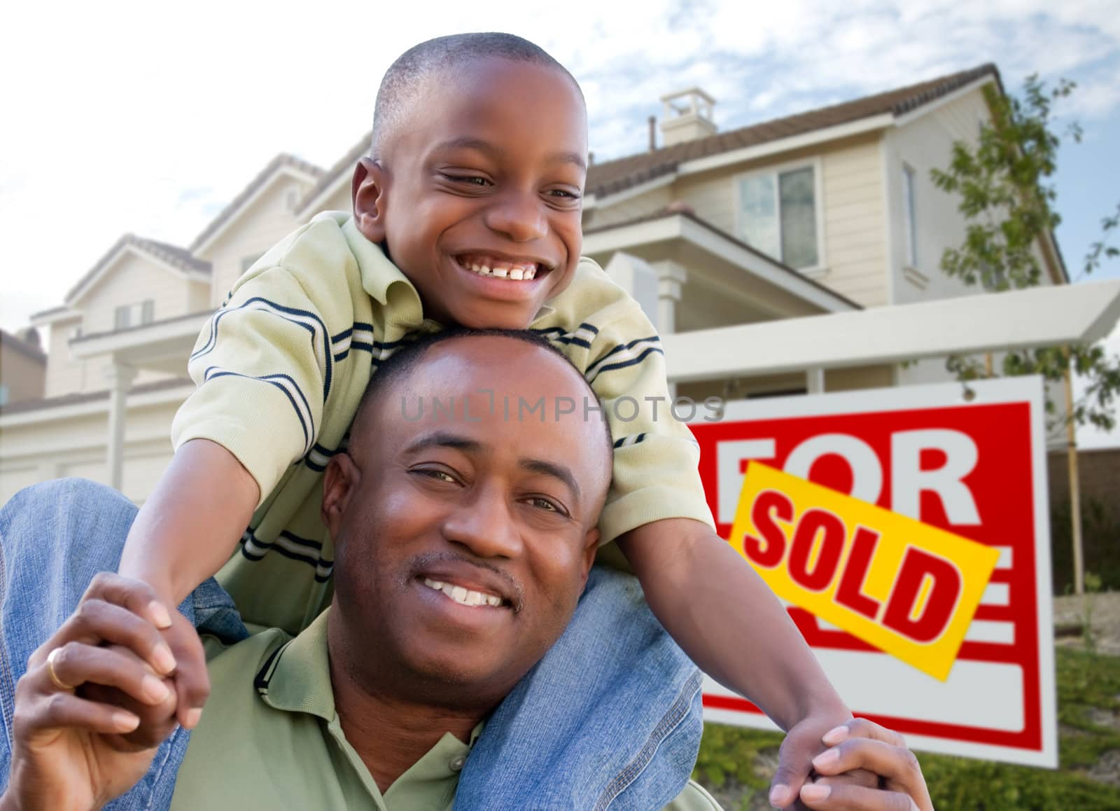 Happy African American Father and Son in Front of New Home and Real Estate Sign.