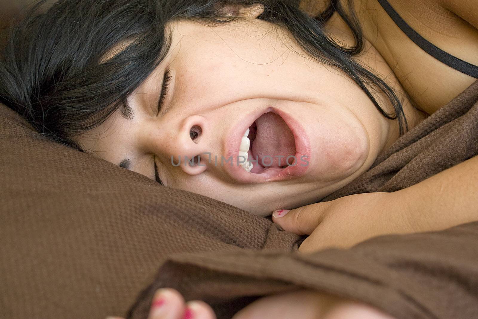 A young brunette woman is yawning as she lays in her bed.