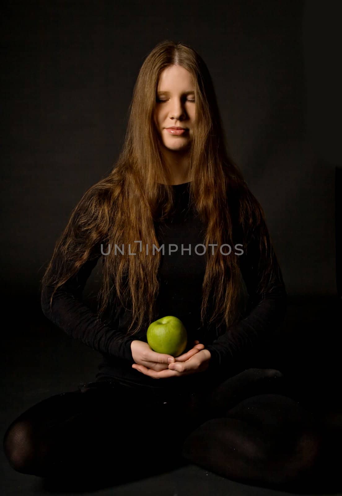 The portrait of a woman with a green apple in her hands, black background