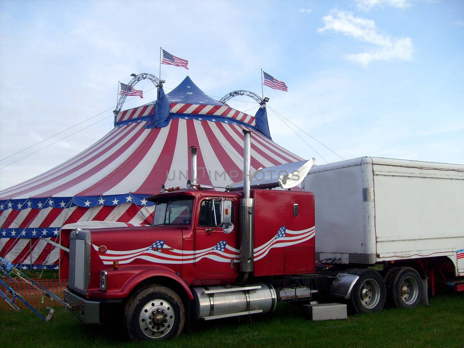 Circus big top tent in field decorated with stars and stripes, big monster truck in foreground.