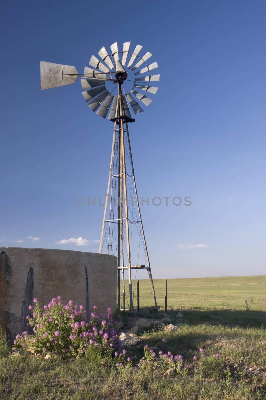 windmill, water pump and concrete tank in shortgrass prairie of  by PixelsAway