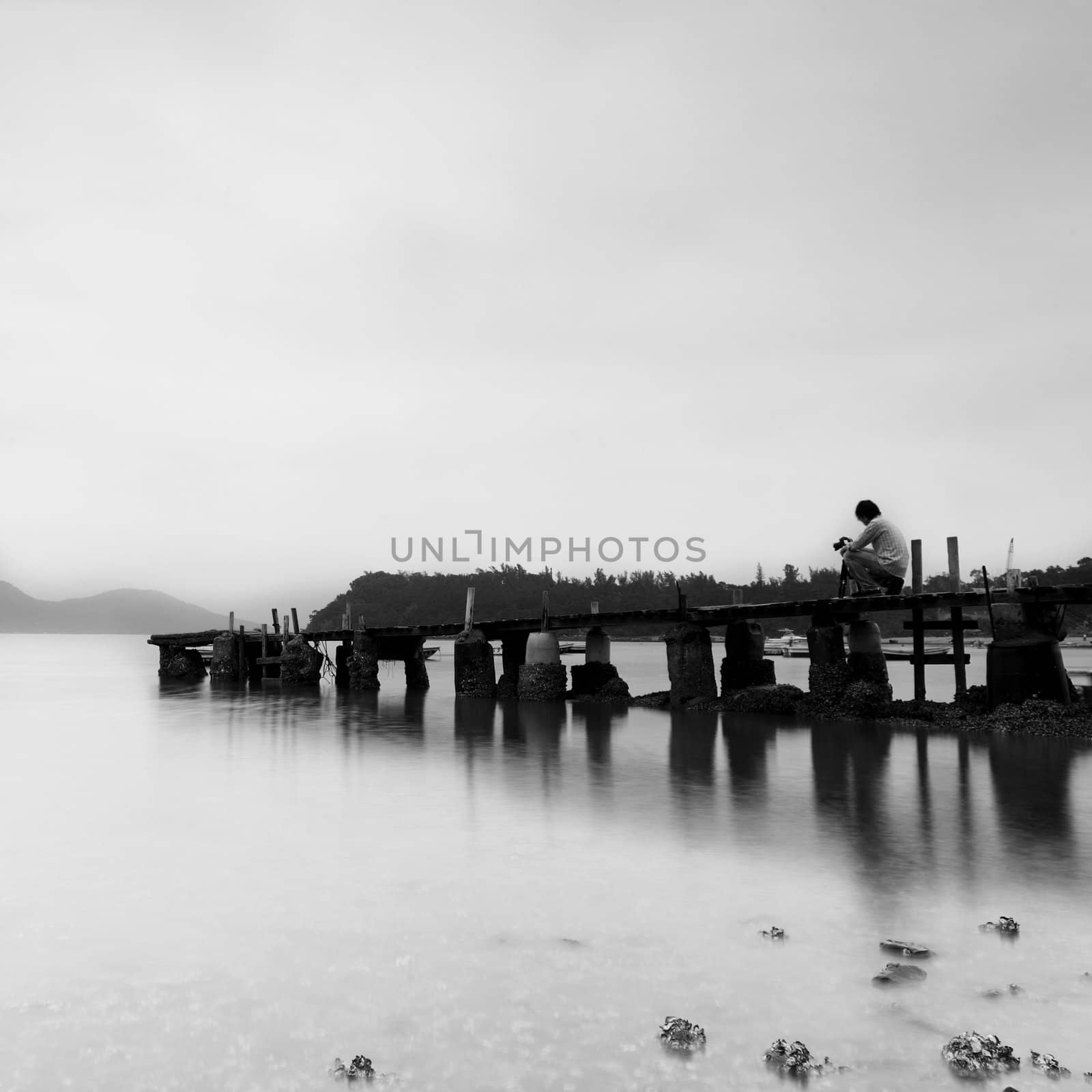 man with camera on a pier and looking at a sea skyline, black and white