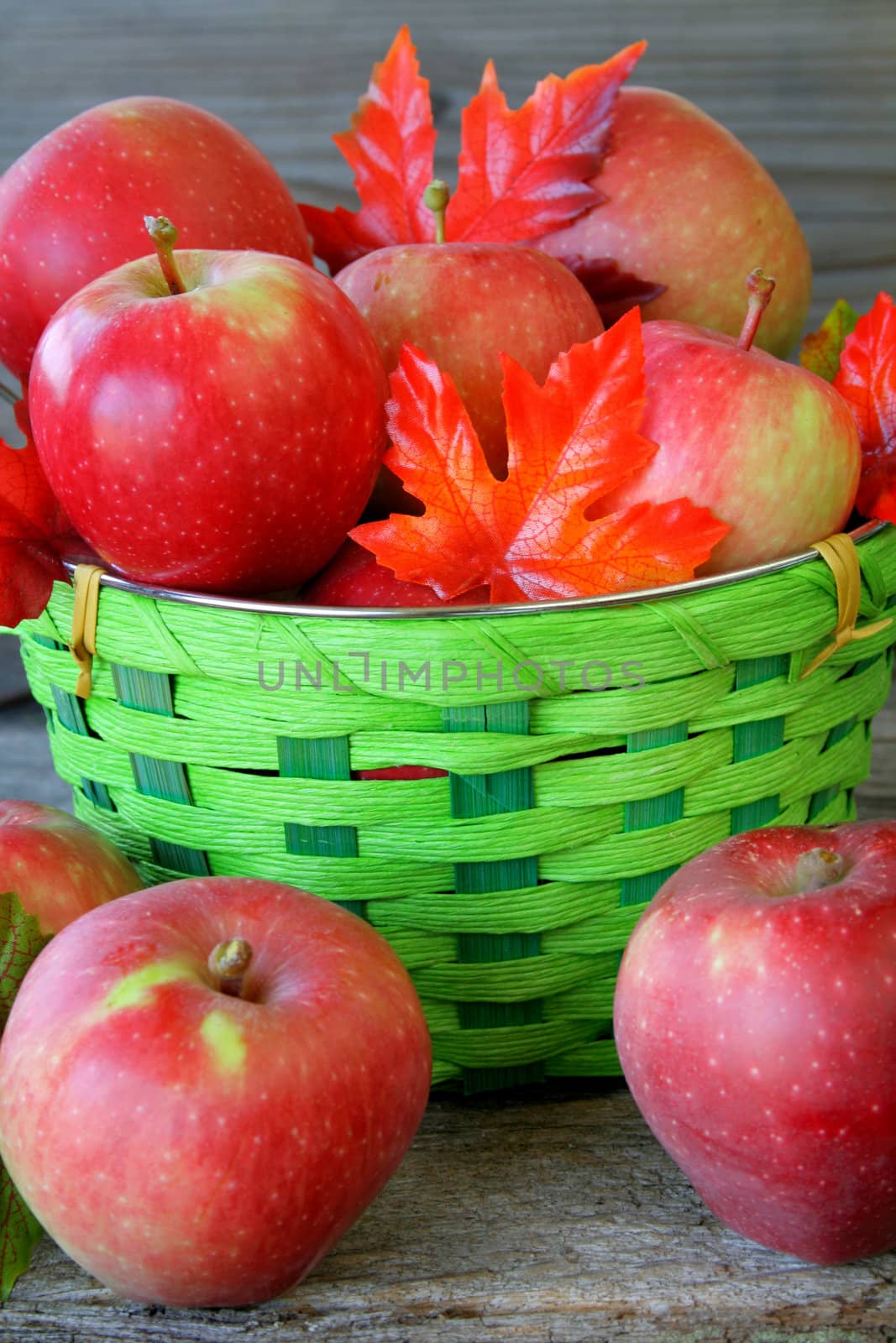 A close up of a basket full of apples with silk fall leaves.