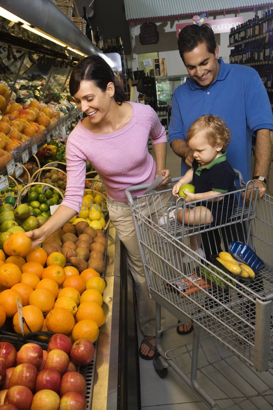 Caucasian mid-adult parents grocery shopping for fruit with male toddler.