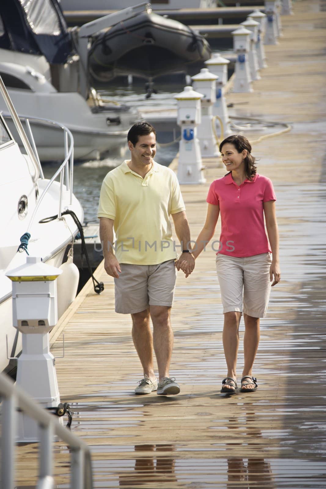 MId-adult Caucasian couple holding hands and walking at harbor.